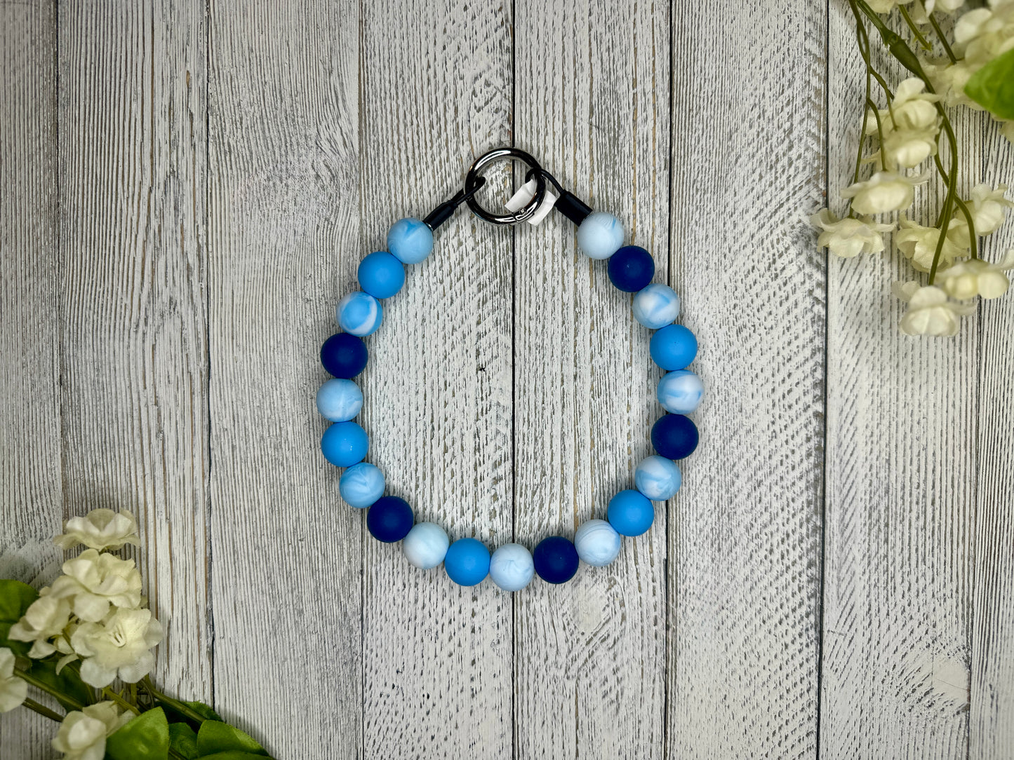 Beaded pet necklace with a blue and white pattern. Displayed on a wooden surface with flowers for decoration. 
