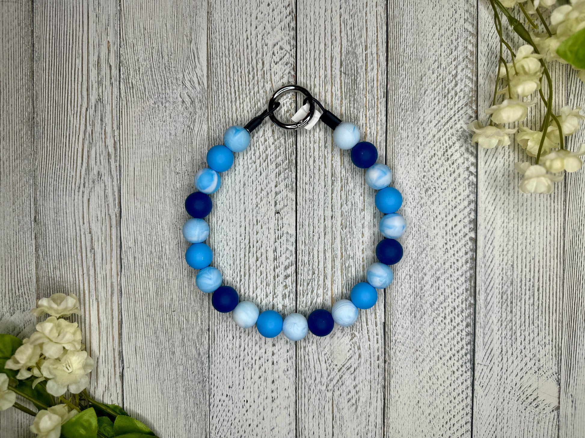 Beaded pet necklace with a blue and white pattern. Displayed on a wooden surface with flowers for decoration. 