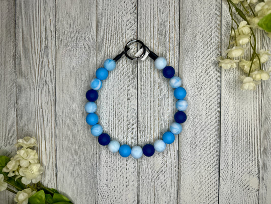 Beaded pet necklace with a blue and white pattern. Displayed on a wooden surface with flowers for decoration. 