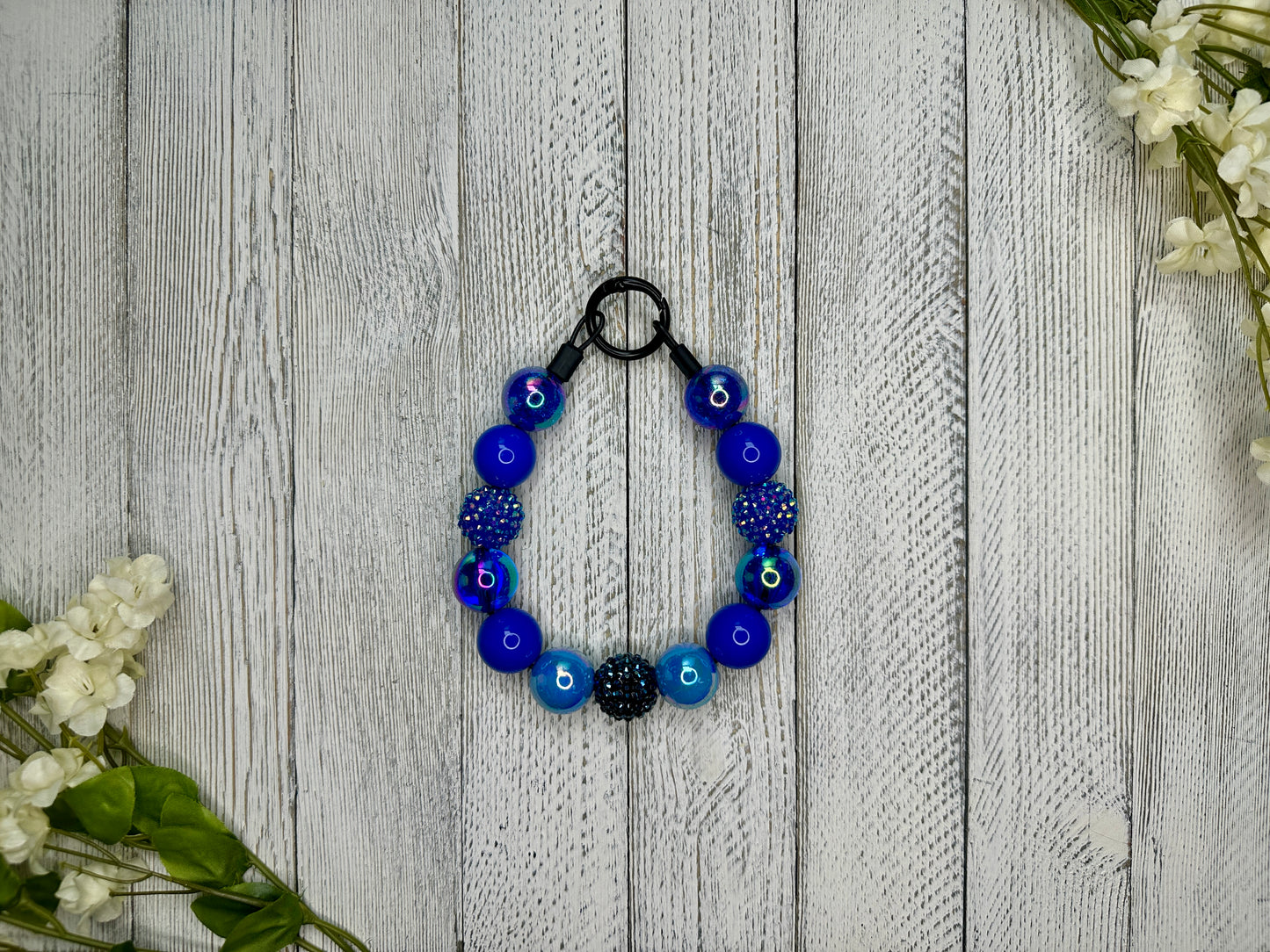 Beaded pet necklace with a navy blue pattern including sparkles. Displayed on a wooden surface with flowers for decoration.
