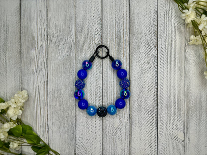 Beaded pet necklace with a navy blue pattern including sparkles. Displayed on a wooden surface with flowers for decoration.
