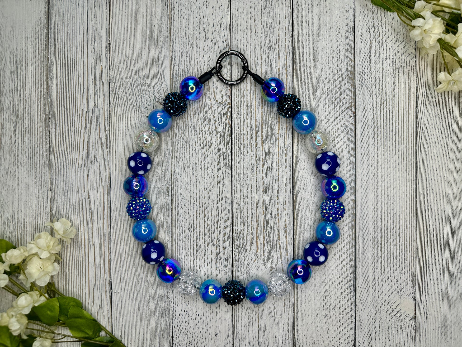 Beaded pet necklace with a navy blue pattern including sparkles and polka dots. Displayed on a wooden surface with flowers for decoration.