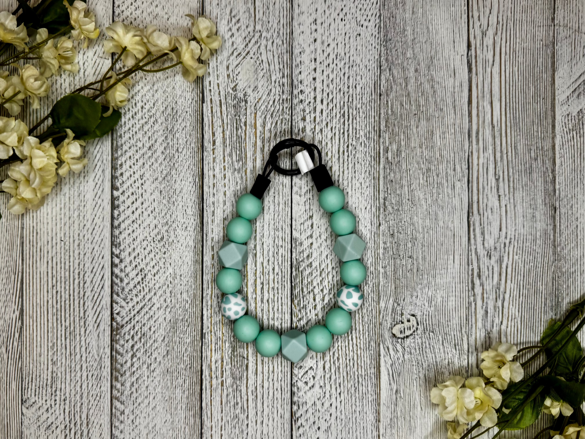 Beaded pet necklace with a seafoam pattern, including polka dots. Displayed on a wooden surface with flowers for decoration. 
