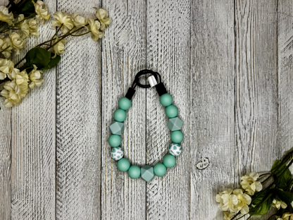 Beaded pet necklace with a seafoam pattern, including polka dots. Displayed on a wooden surface with flowers for decoration. 