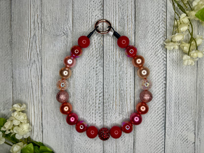 Beaded pet necklace with a red sunset pattern, including sparkles. Displayed on a wooden surface with flowers for decoration. 
